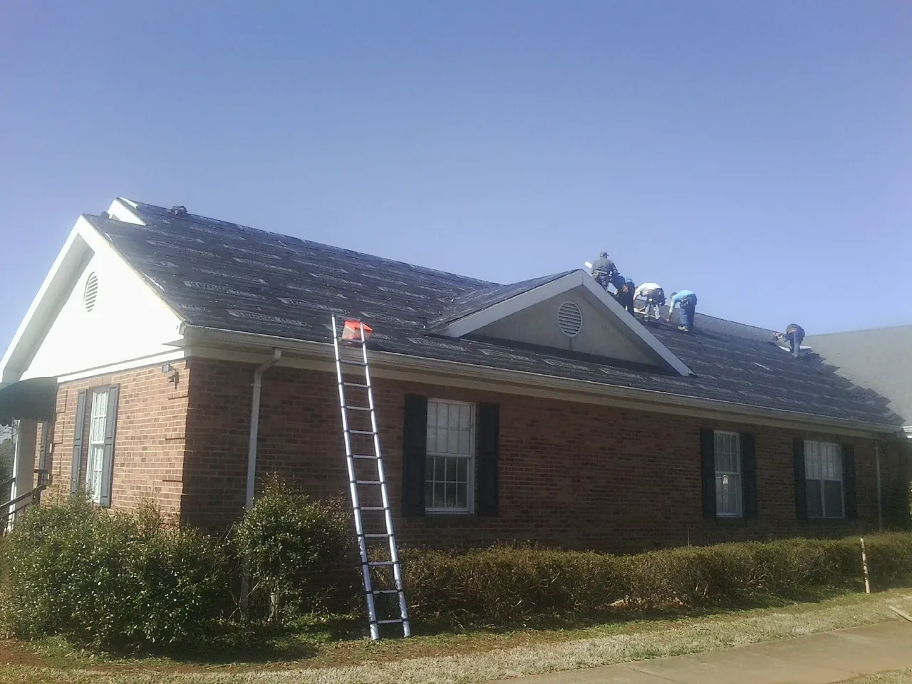 Crew tearing shingles off a brick ranch roof with a ladder set — Emergency Roof Repair work by our crew in Newcomerstown