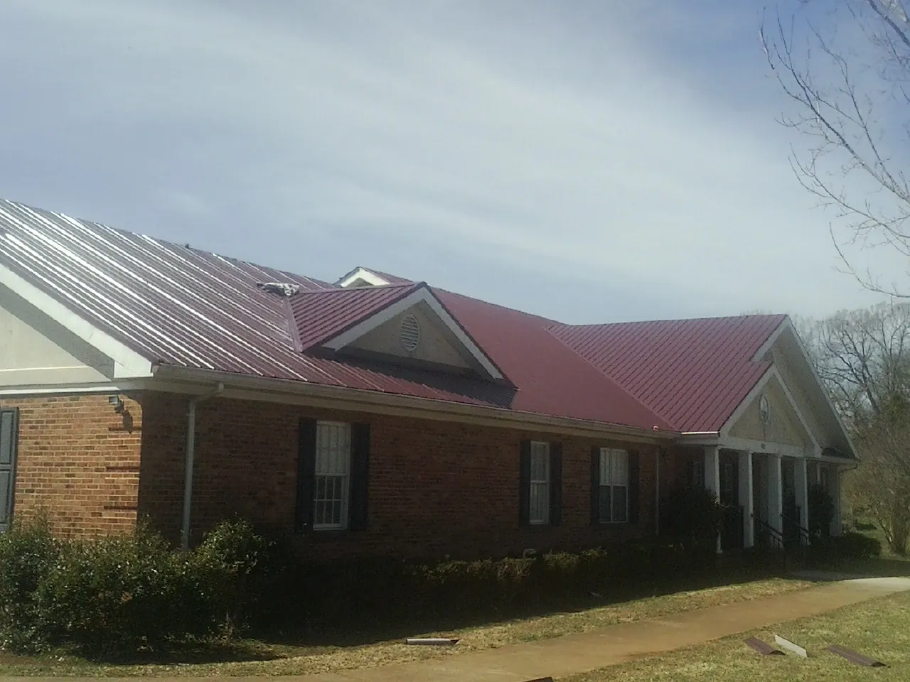Red metal roof with gabled entries on a long brick building, from a Hail Damage Roof Repair job in Newcomerstown