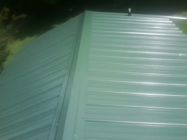 New green metal panels meeting at the ridge of a roof — Flat Roof Repair work by our crew in Newcomerstown