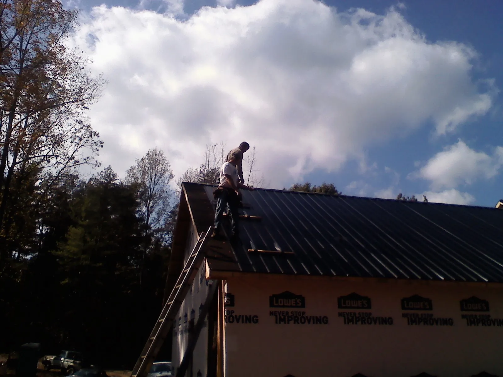 Roofer fastening dark metal panels high against a cloudy sky, from a Roof Inspection job in Newcomerstown