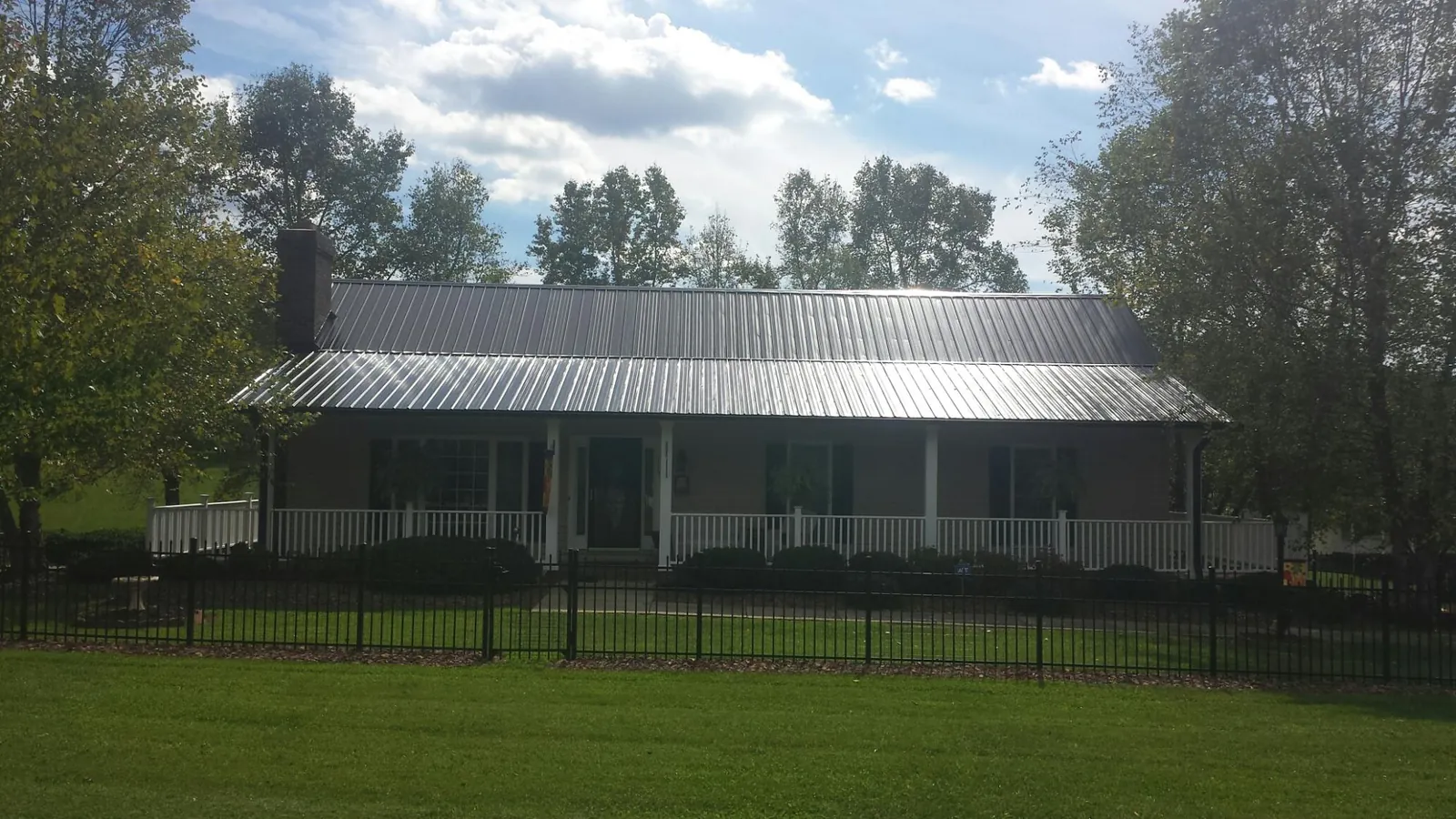 Gray metal roof on a brick ranch with a full width front porch — Gutter Guard Installation work by our crew in Newcomerstown