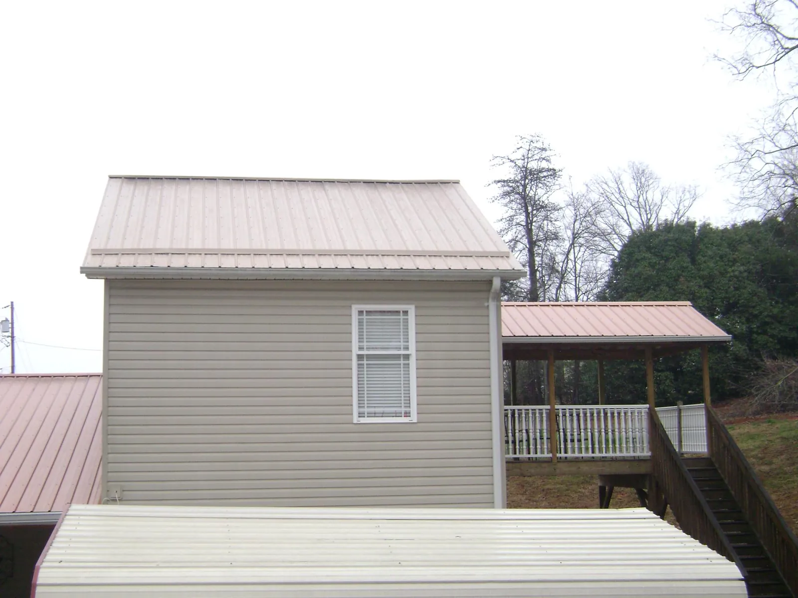Tan metal roofs on a two story addition and attached porch, from a Roof Replacement job in Newcomerstown